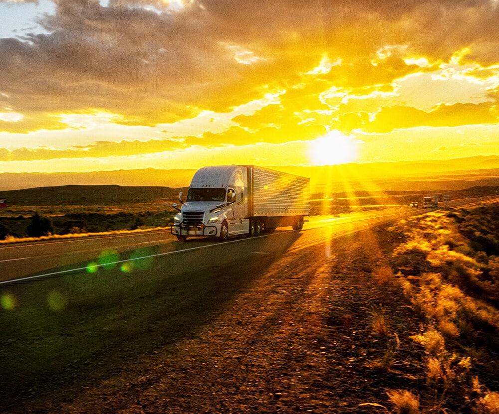 A semi truck driving on a highway at sunset.