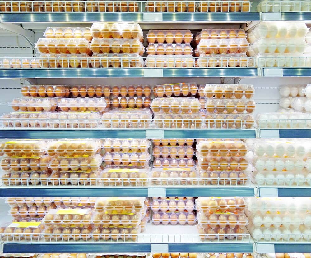 Refrigerated shelves of brown and white eggs in plastic egg cartons.