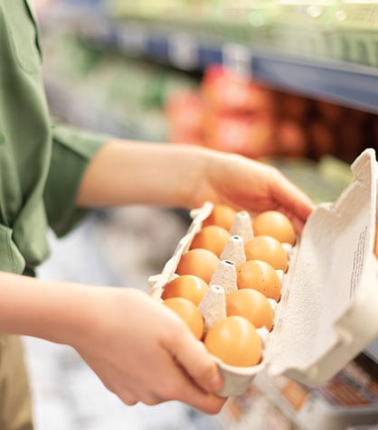 A woman in a green shirt holding an open carton of brown eggs.