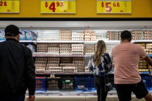 Image of shoppers in a grocery store observing lower egg prices, featured in an article about Eggs Unlimited. The headline 'Good news about breakfast: egg prices are dropping' highlights the positive trend in egg costs.
